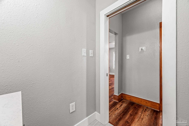 hallway featuring baseboards, wood finished floors, and a textured wall