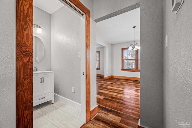 bathroom featuring a notable chandelier, a textured wall, vanity, wood finished floors, and baseboards