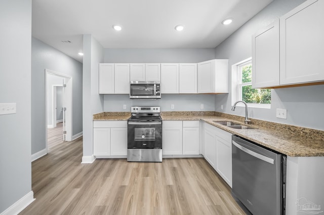 kitchen featuring appliances with stainless steel finishes, sink, dark stone countertops, white cabinets, and light hardwood / wood-style flooring