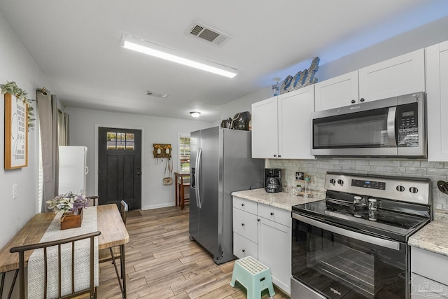 kitchen with white cabinets, backsplash, light stone counters, and appliances with stainless steel finishes