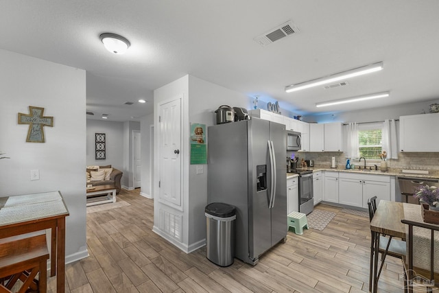 kitchen featuring appliances with stainless steel finishes, sink, light hardwood / wood-style floors, decorative backsplash, and white cabinetry