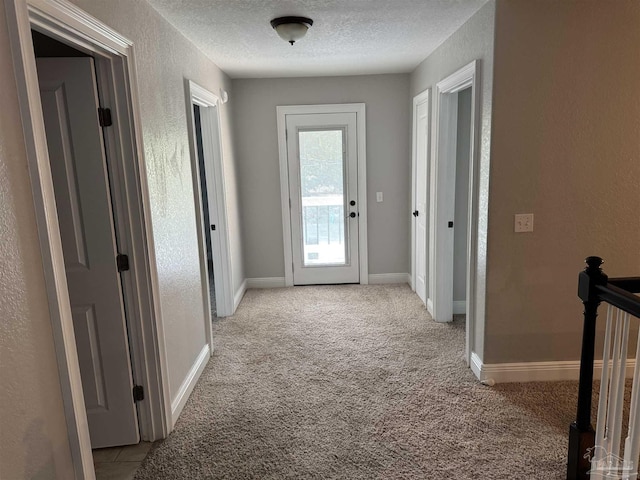 hallway with light colored carpet and a textured ceiling