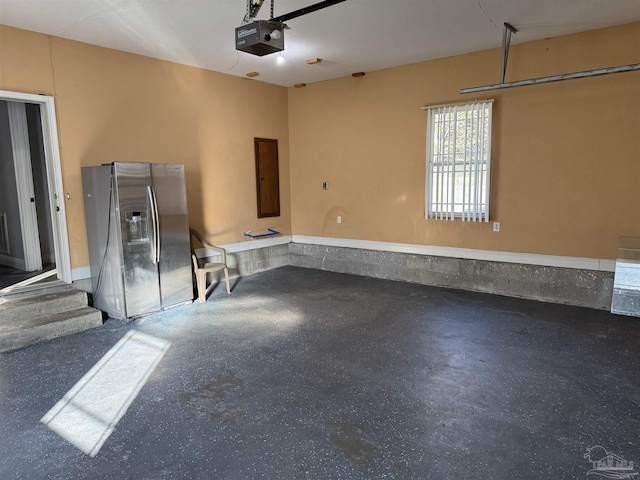 garage with a garage door opener and stainless steel refrigerator with ice dispenser