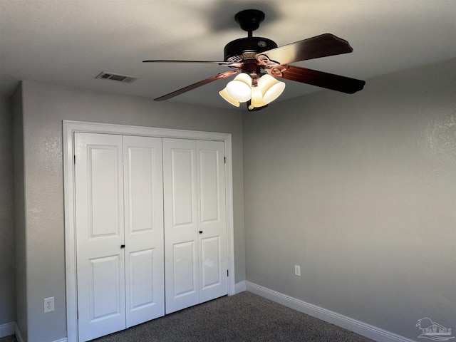 unfurnished bedroom with ceiling fan, dark carpet, and a closet