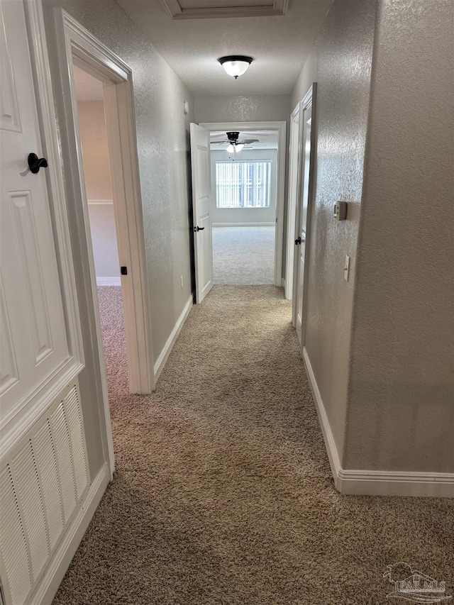 hallway featuring light colored carpet and a textured ceiling