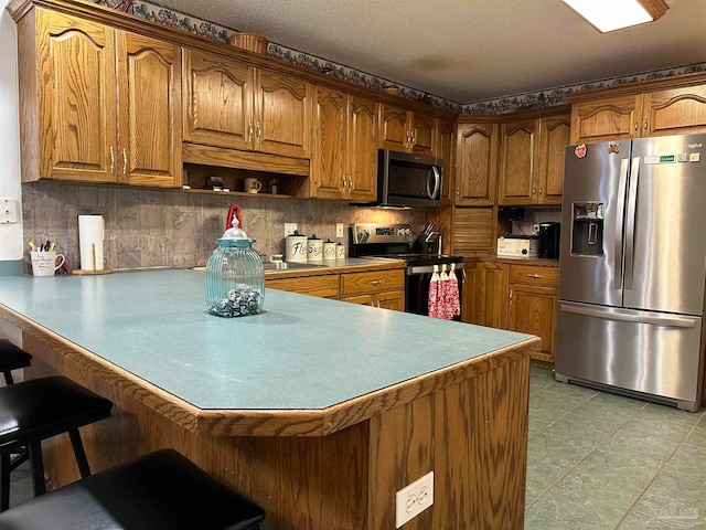 kitchen with appliances with stainless steel finishes, tasteful backsplash, a kitchen bar, and kitchen peninsula