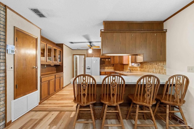 kitchen with kitchen peninsula, backsplash, sink, white refrigerator with ice dispenser, and light hardwood / wood-style floors