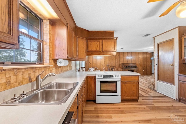 kitchen with electric range, sink, a textured ceiling, wooden walls, and light wood-type flooring