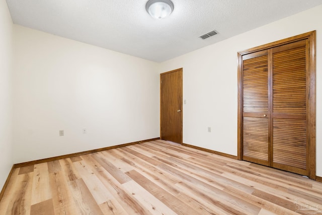 unfurnished bedroom featuring a textured ceiling, light hardwood / wood-style flooring, and a closet