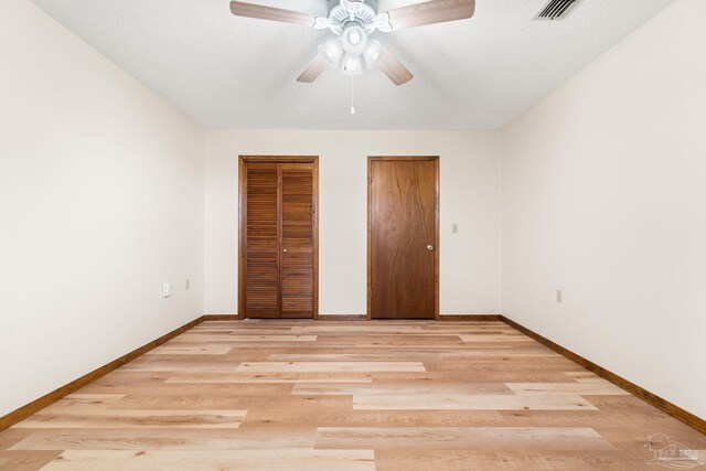 unfurnished bedroom featuring ceiling fan, light hardwood / wood-style floors, and multiple closets