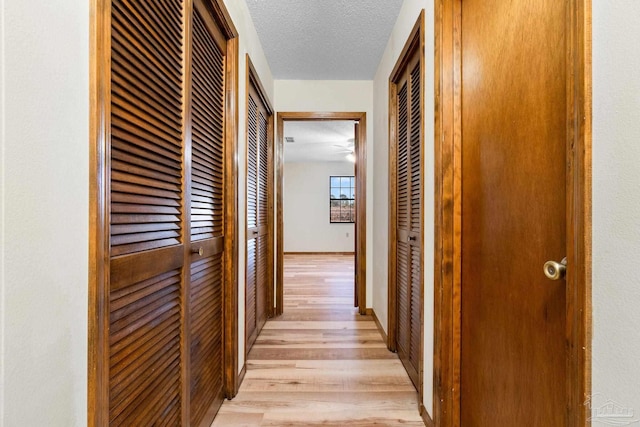 hallway with a textured ceiling and light hardwood / wood-style floors