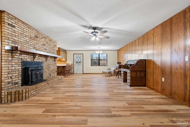 unfurnished living room featuring a textured ceiling, light hardwood / wood-style floors, a wood stove, and wood walls