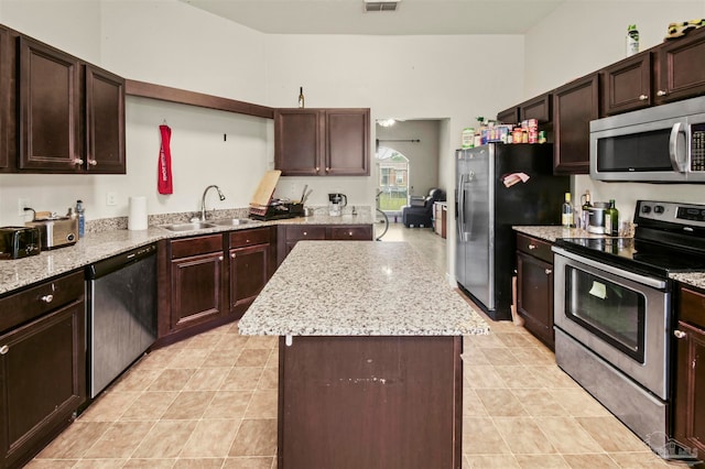 kitchen with appliances with stainless steel finishes, light stone counters, a kitchen island, and sink