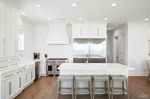 kitchen featuring sink, a breakfast bar area, premium range hood, high quality appliances, and a kitchen island with sink