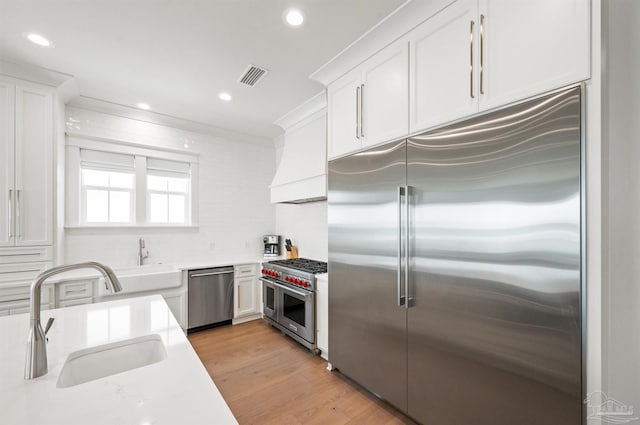 kitchen featuring sink, white cabinets, light hardwood / wood-style flooring, custom exhaust hood, and high quality appliances