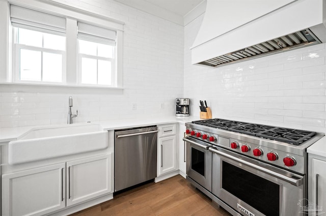 kitchen featuring stainless steel appliances, tasteful backsplash, custom range hood, white cabinetry, and sink