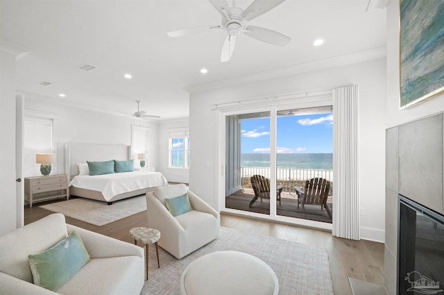 bedroom featuring access to outside, a large fireplace, light hardwood / wood-style floors, crown molding, and ceiling fan