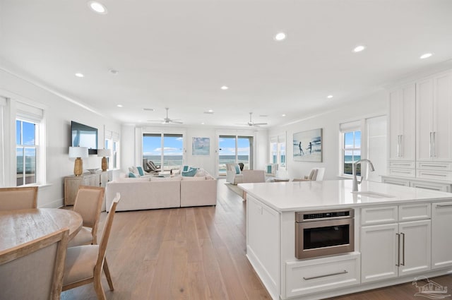 kitchen with white cabinets, a kitchen island with sink, wall oven, ceiling fan, and sink