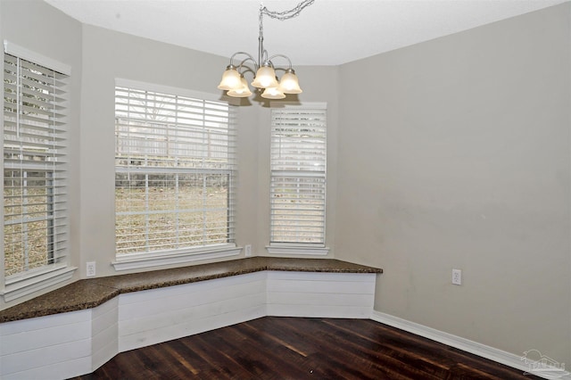 unfurnished dining area with a chandelier, dark wood-type flooring, and baseboards