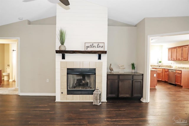 living area with dark wood-style floors, lofted ceiling, a tiled fireplace, a ceiling fan, and baseboards