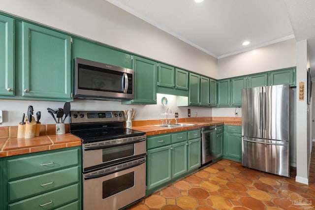 kitchen featuring tile counters, appliances with stainless steel finishes, crown molding, a sink, and recessed lighting