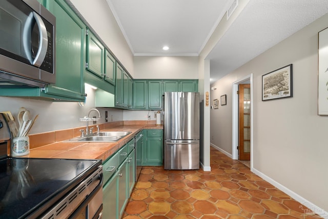 kitchen with appliances with stainless steel finishes, green cabinetry, a sink, and ornamental molding