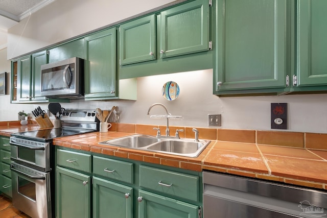 kitchen featuring appliances with stainless steel finishes, green cabinetry, a sink, and ornamental molding