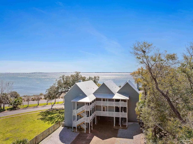 exterior space with metal roof, a water view, fence, stairs, and a front lawn