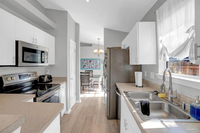 kitchen with light countertops, light wood-style flooring, appliances with stainless steel finishes, a sink, and a chandelier