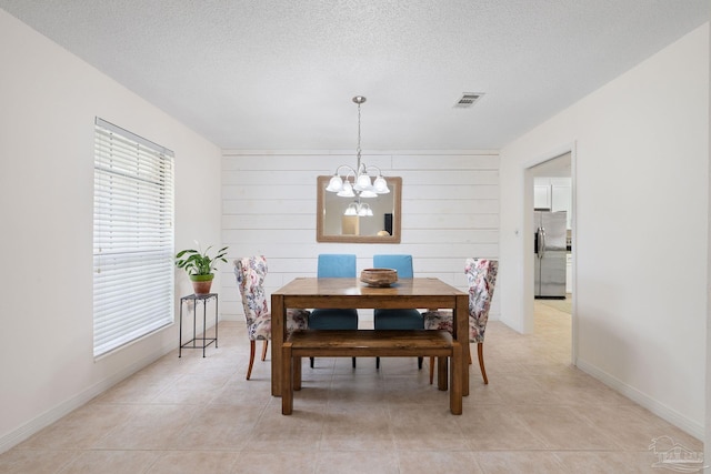 dining area with a textured ceiling, light tile patterned floors, baseboards, and a notable chandelier