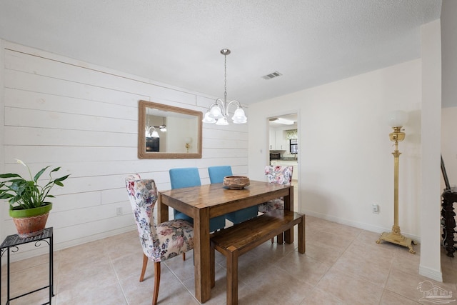 dining space with a textured ceiling, light tile patterned floors, visible vents, baseboards, and an inviting chandelier