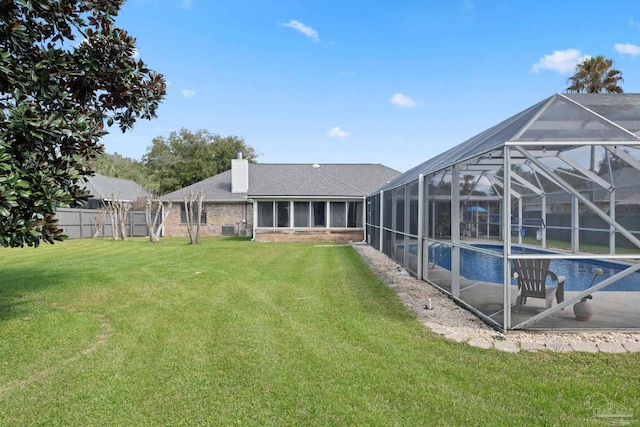 back of property featuring a chimney, a lawn, fence, a lanai, and an outdoor pool