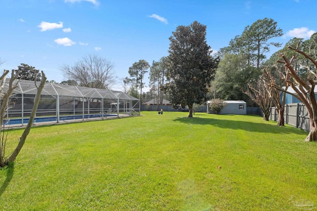 view of yard featuring a lanai, a fenced backyard, a pool, and an outbuilding