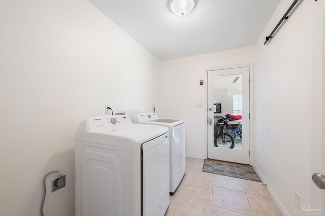 clothes washing area with a textured ceiling, a barn door, light tile patterned flooring, laundry area, and separate washer and dryer