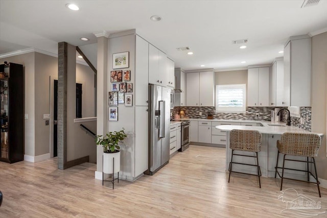 kitchen with a peninsula, a sink, a kitchen breakfast bar, high quality appliances, and light wood-type flooring