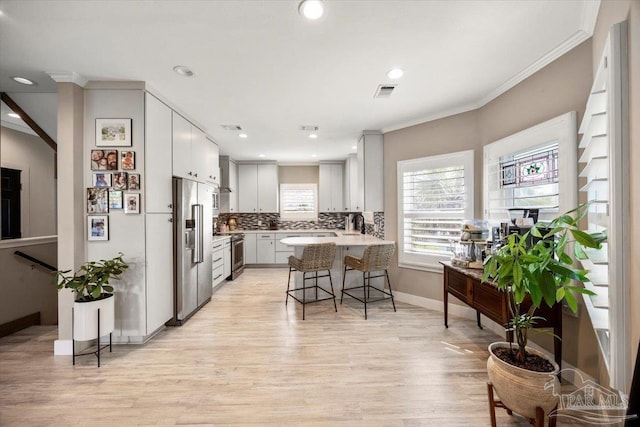 kitchen featuring a peninsula, ornamental molding, light countertops, appliances with stainless steel finishes, and a kitchen breakfast bar