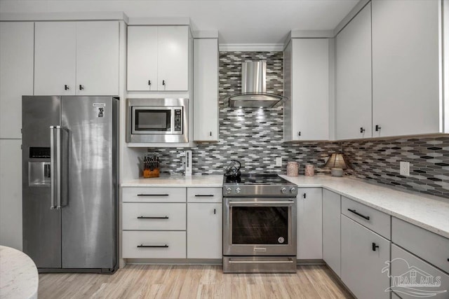 kitchen featuring light wood-style floors, stainless steel appliances, tasteful backsplash, and wall chimney range hood