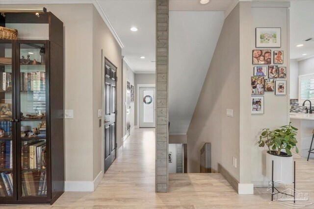 hall with light wood-style flooring, baseboards, and ornamental molding