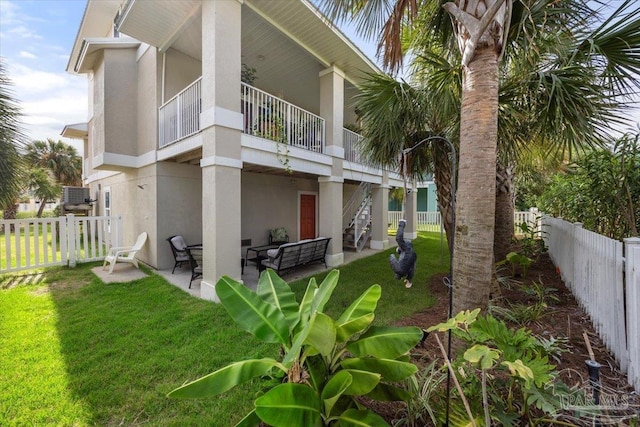 rear view of house featuring stucco siding, a lawn, a fenced backyard, and a patio area