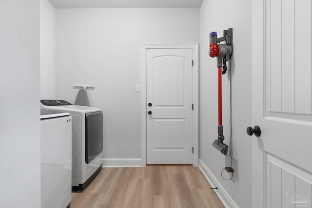 clothes washing area with laundry area, washing machine and clothes dryer, light wood-style flooring, and baseboards