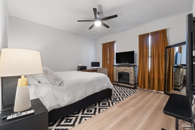 bedroom with a ceiling fan, a stone fireplace, and wood finished floors