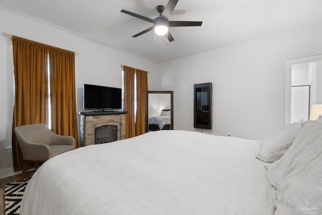 bedroom featuring a stone fireplace, a ceiling fan, and baseboards