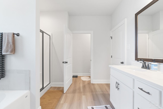 full bath featuring a garden tub, a stall shower, vanity, wood finished floors, and baseboards