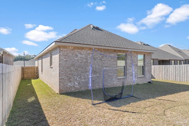 rear view of house with roof with shingles, brick siding, a lawn, and a fenced backyard