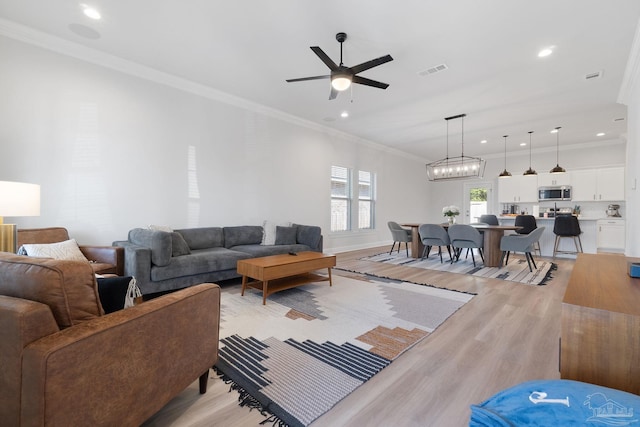 living area featuring light wood-style flooring, recessed lighting, visible vents, and crown molding