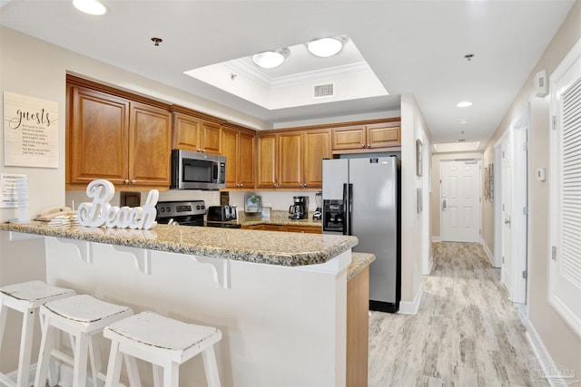 401 E Beach Blvd Unit 1207, Gulf Shores, AL 36542 - kitchen with appliances with stainless steel finishes, a peninsula, a kitchen bar, light wood-type flooring, and a tray ceiling