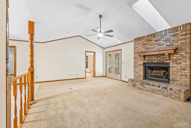 unfurnished living room featuring lofted ceiling with skylight, carpet flooring, ceiling fan, and a fireplace