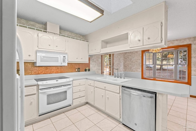 kitchen featuring light tile patterned flooring, sink, white cabinets, kitchen peninsula, and white appliances