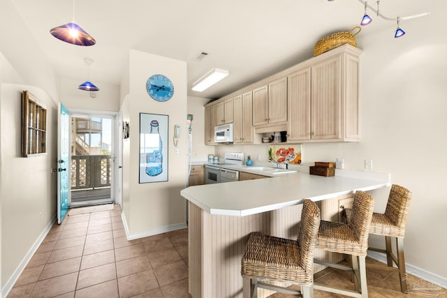 kitchen featuring white appliances, a breakfast bar, pendant lighting, light brown cabinets, and kitchen peninsula