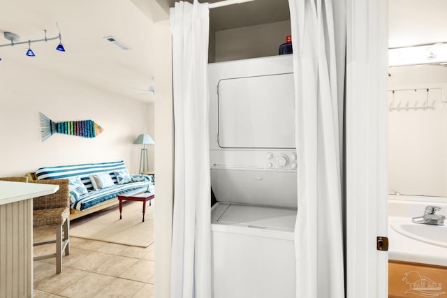 laundry room with light tile patterned floors, stacked washer and clothes dryer, and sink